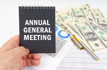 In the man's hand is a notepad with the inscription - ANNUAL GENERAL MEETING, in the background a pen and dollars