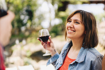 Happy young woman talking carefree with friends holding a glass of red wine - people lifestyle concept