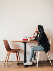 Women working on a table with her laptop inside a minimalist and elegance coffee shop. Wooden table with 2 chairs and 1 girl sitting studying.