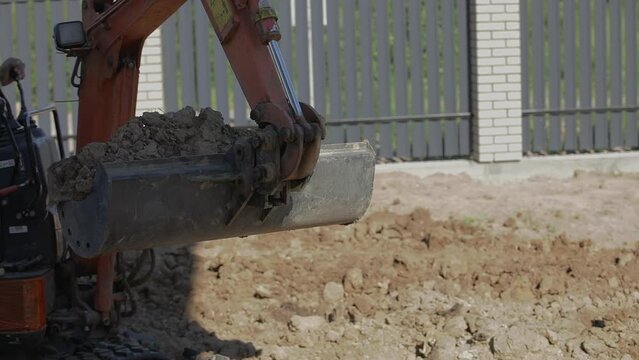 A mini excavator with a bucket is leveling a piece of land. landscape preparation
