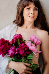 a woman topless wearing a white shirt on shoulder with a bouquet of peonies.