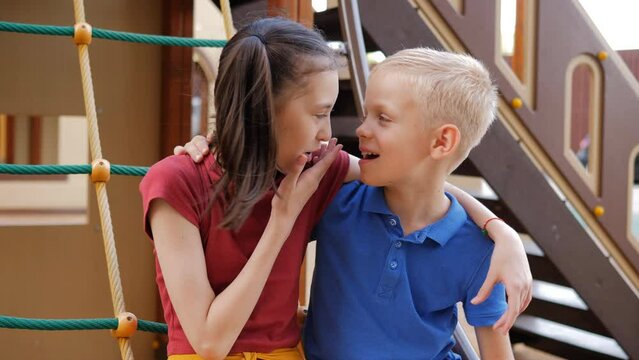 A boy and a girl are sitting on the playground in an embrace talking and laughing. Romance and first love concept.