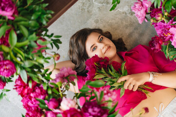 an attractive young woman in a pink blouse with peony flowers on the floor. 