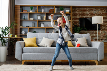 Happy little girl wearing red headphones dancing and singing, jumping on a floor. Cute child enjoy...