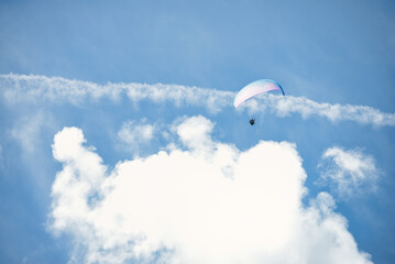 Single paraglider with a blue and purple canopy in front of big white clouds and a faded-out...
