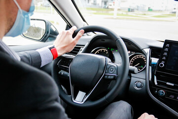 young man driver in a medical mask and business suit driving a new car
