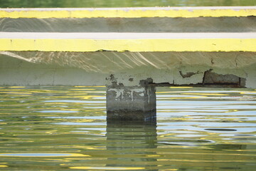Stara betonowa opora mostu nad wodą z odstającej farbą - obrazy, fototapety, plakaty