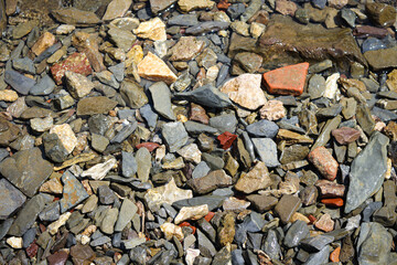 Multi-colored sea stones in the water. Wet drops in the sea. Stones of various shapes. Natural background