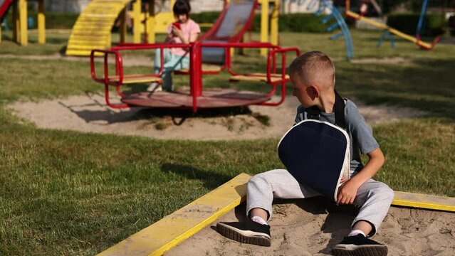 crying child with broken limb arm sits outdoors and looking how kid girl is playing on playground. concept of health accident, and medical. the worst summer vacation