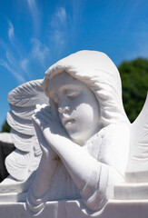 White angel close up with both hands together against a blue sky with clouds. White angel with sleeping gesture in vertical orientation.