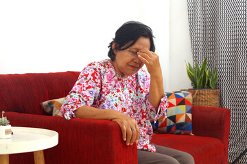 Senior asian woman with headache or dizzy or migraine while sitting on sofa at home.