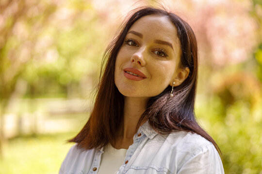 Portrait of beautiful young brunette woman looking and smiling to camera. At park.