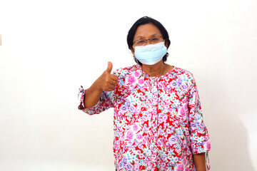 Senior elderly woman standing and wearing face mask while showing thumbs up. Isolated on white