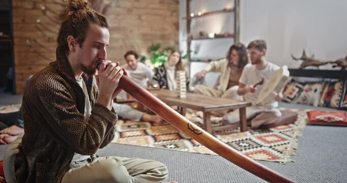 Group of hippie friends playing assorted musical instruments. Group of hippie friends playing assorted musical instruments with focus to a young man playing a didgeridoo