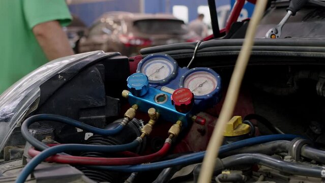 Under hood of open car lies system of manometers for refueling air conditioner. Blue pressure gauges with red and blue knobs in process of service maintenance of vehicle system.