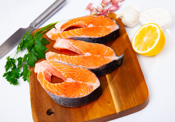 Fresh sliced steaks of salmon with herbs and lemon on a wooden kitchen board