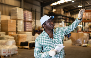 African-american man warehouse worker gesturing with hand, holding documents.