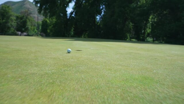 Close up following golf ball as putter putts on green and ball goes in the hole