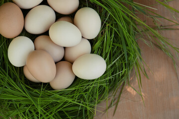 Nest made of green grass with fresh raw eggs on wooden table, top view