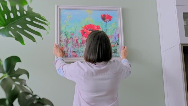 Woman hanging floral art framed at home on the wall