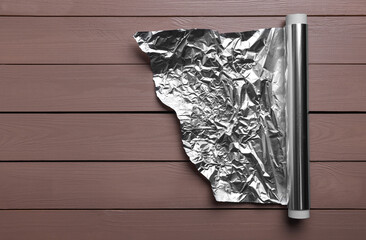 Roll of aluminum foil on wooden table, top view. Space for text