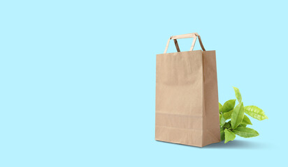 Paper shopping bag and green leaves on cyan background, space for text. Eco friendly lifestyle