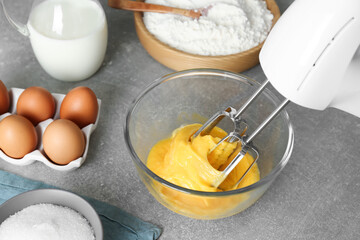 Beating eggs in glass bowl with mixer on light grey table
