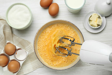 Beating eggs in bowl with mixer at white wooden table, flat lay