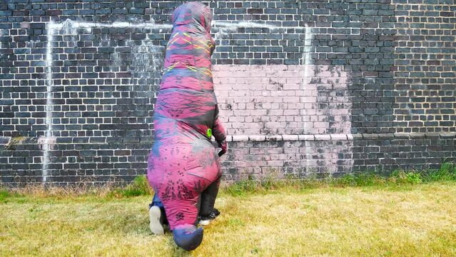 Funny dancing prehistoric dinosaur costume as bubbles float against brick wall