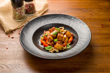 Naklejka premium fried eggplant in sweet sour sauce with tomatoes and cilantro on black plate