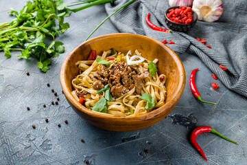 fried Udon with beef and vegetables on wooden bowl on grey table