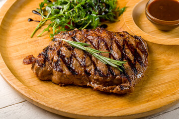 juicy Ribeye steak on wooden plate with aragula, tomatoes and pepper sauce macro close up