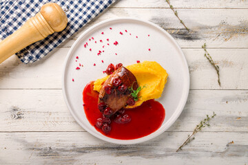 Duck breast with berry sauce and mashed potatoes on white plate on white wooden table top view