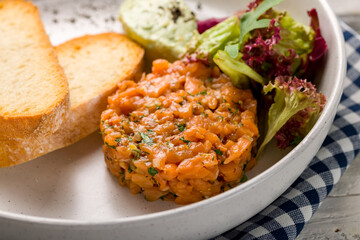 salmon Tartar on plate with mix salad and fried croutons on a plate on white wooden table macro close up