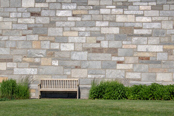 outdoor bench with rock brick wall shrubs and green grass lawn
