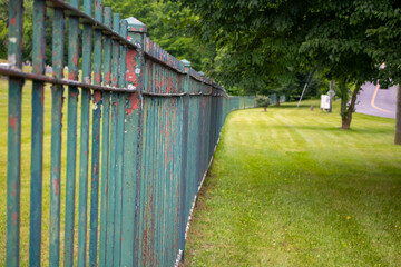 long perspective view of green painted cast iron fence with trees and green grass lawn
