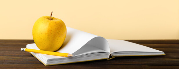 School notebook with apple and pencil on table against yellow background