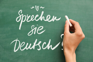 Woman's hand with chalk writing text SPRECHEN SIE DEUTSCH? (DO YOU SPEAK GERMAN?) on blackboard