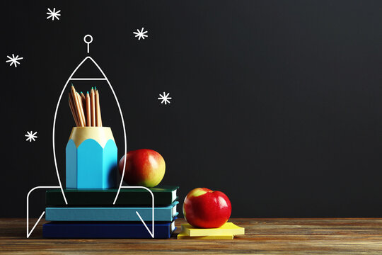 Drawn rocket with books, apples and school stationery on table against dark background with space for text