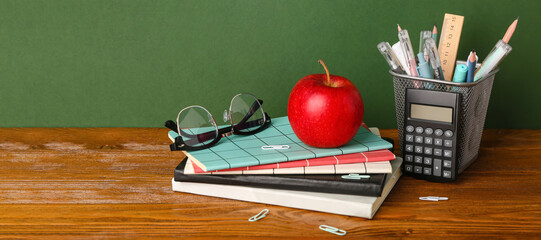 School stationery with apple and eyeglasses on table against green background