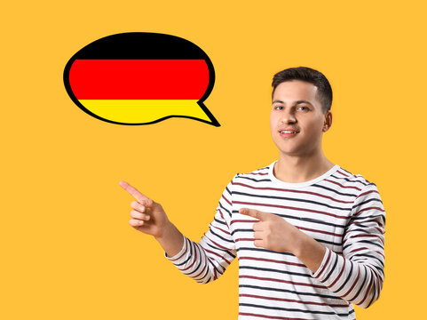 Portrait of young man pointing at speech bubble on yellow background. Concept of speaking German