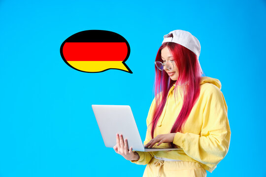 Young female student with bright unusual hair holding laptop on blue background. Concept of studying German online