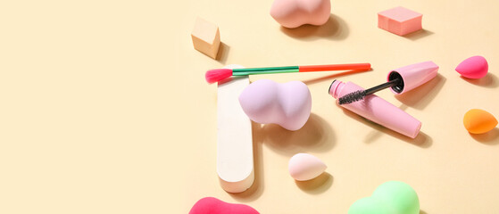 Makeup sponges, brush and decorative cosmetics on beige background with space for text