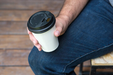 Seated person holding a paper cup of coffee

