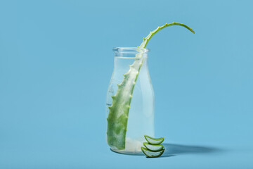 Glass bottle of aloe juice with leaves on blue background