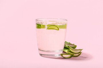 Glass of aloe juice with leaves on pink background