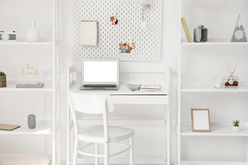 Interior of light office with workplace, pegboard and shelving units