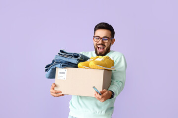 Happy young man with credit card and parcel on lilac background. Online shopping