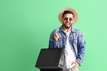 Handsome man with credit card and shopping bags on green background