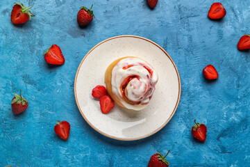 Plate with strawberry cinnamon roll and cream on blue background